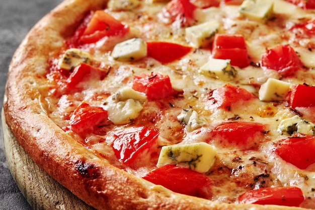 Thin pizza with mozzarella tomatoes blue cheese and dried basil on wooden cutting board