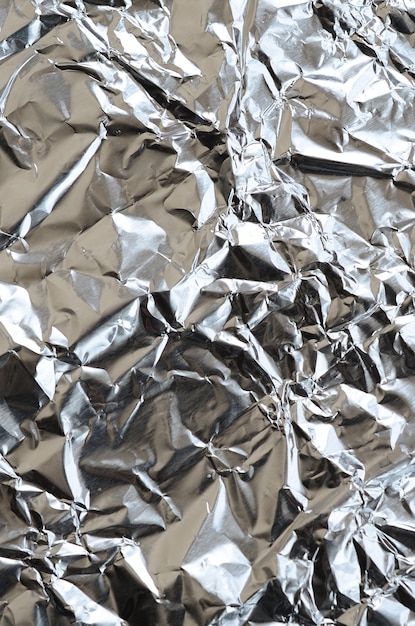 Thin wrinkled sheet of crushed tin aluminum silver foil background 