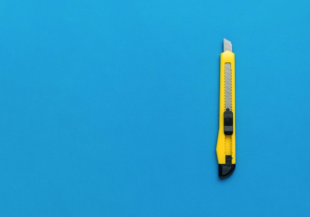 A thin yellow paper knife on a bright blue background Minimalistic concept