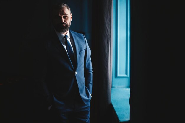 Thinking about Thoughtful man in full suit looking away through the window while standing indoors