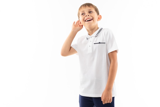 Thinking boy with bangs in a white t-shirt listens on white with copy space