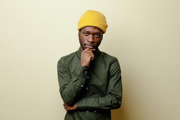 Thinking grabbed chin young african american male in hat wearing green shirt isoloated on white background