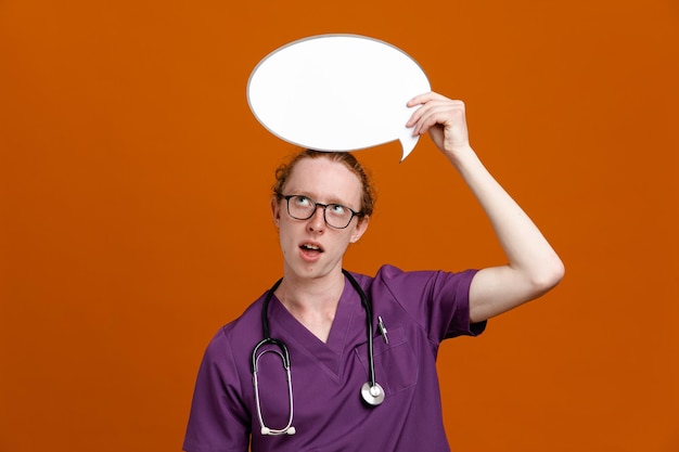 thinking holding bubble young male doctor wearing uniform with stethoscope isolated on orange background