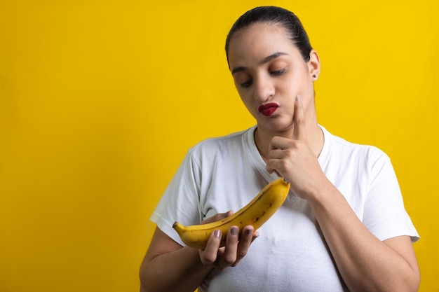 thinking latin woman with banana in hands, on yellow background