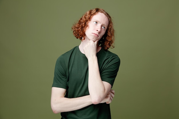 Thinking looking side putting hand on chin young handsome guy wearing green t shirt isolated on green background