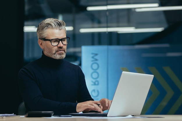 Thinking man inside office at work mature adult businessman looking at laptop screen gray haired