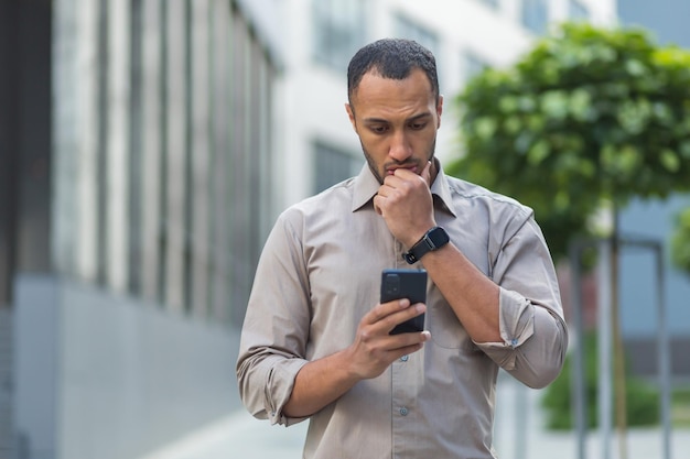 Thinking and sad muslim businessman reading message from smartphone man outside office building