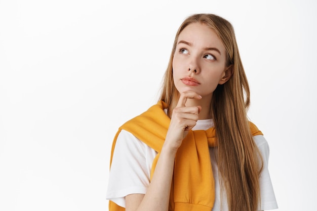 Thinking woman making choice touching chin pensive looking at upper left corner thoughtful reading sign promotional text with pondering face standing over white background