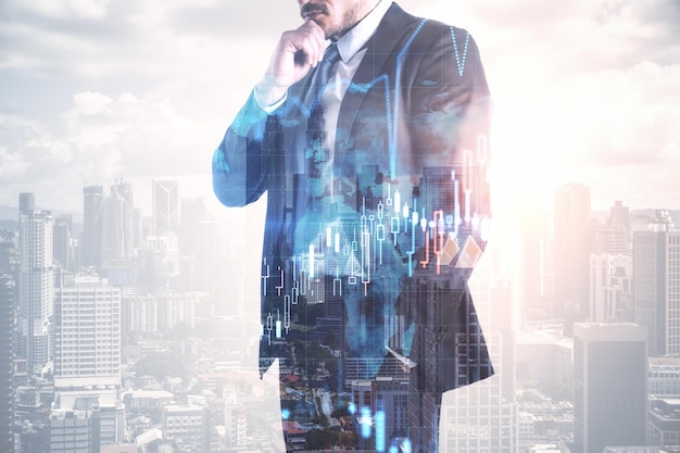 Thinking young european businessman in suit standing on abstract bright city background with forex chart and mockup place Finance trade and success concept Double exposure