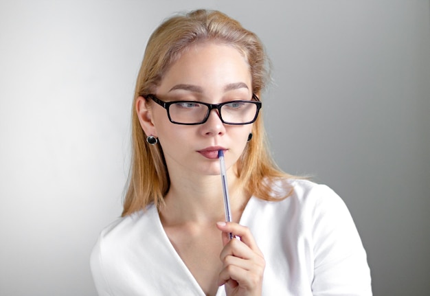 Thinking young woman holding pen on lips