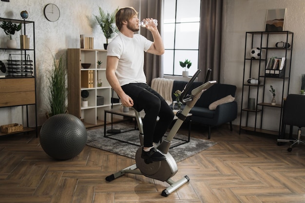 Thirsty handsome young sports bearded caucasian man in sportswear drinking fresh water