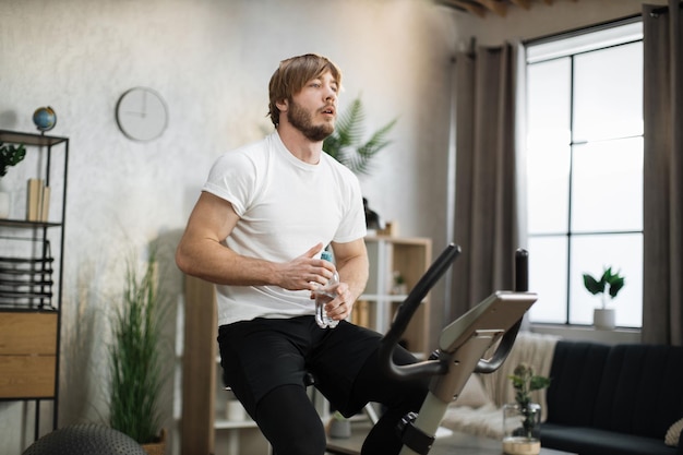 Thirsty handsome young sports bearded caucasian man in sportswear drinking fresh water