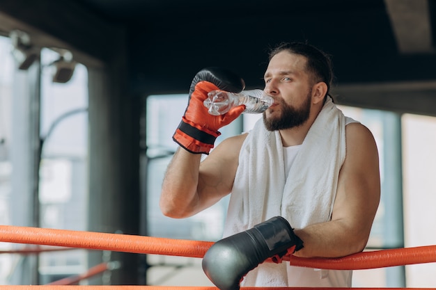 Thirsty male boxer taking a break drinking from the water bottle after training in gym. 