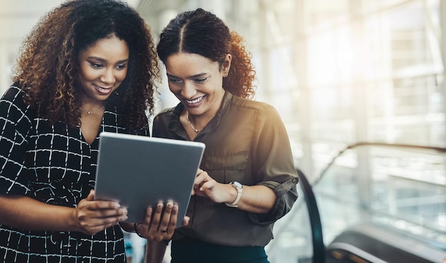 This app will work perfectly for us Cropped shot of two attractive businesswomen using a digital tablet together while standing in a modern workplace