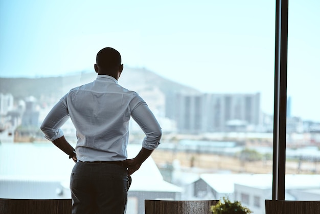 This city inspires me to keep upping my game Rearview shot of a businessman looking out the window in an office