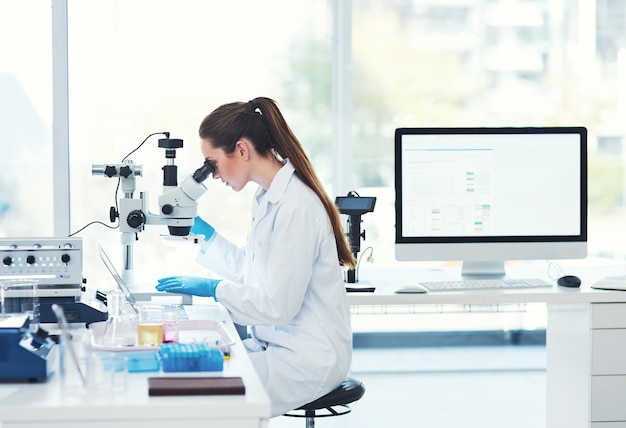 This is all in a days work Cropped shot of a focused young female scientist looking through a microscope while doing tests inside of a laboratory