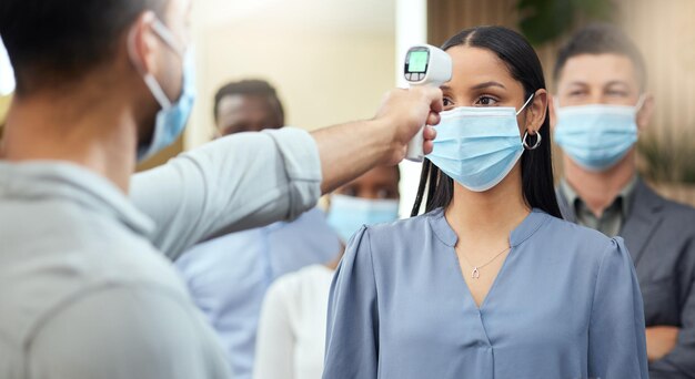 This is how we do business now Cropped shot of an attractive young businesswoman wearing a mask and having her temperature taken while standing at the head of a queue in her office