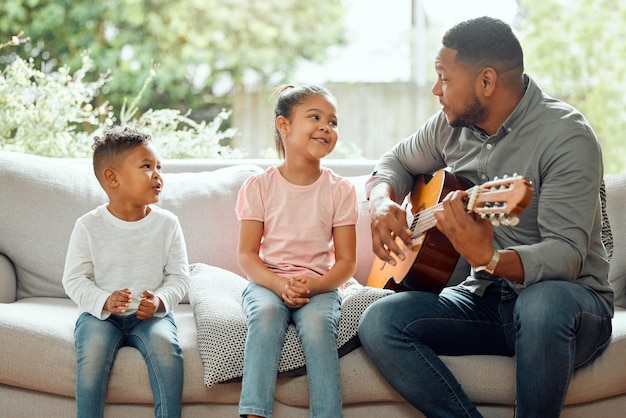 This is moms favourite song Shot of a young father teaching his kids how to play the guitar while sitting on the sofa at home