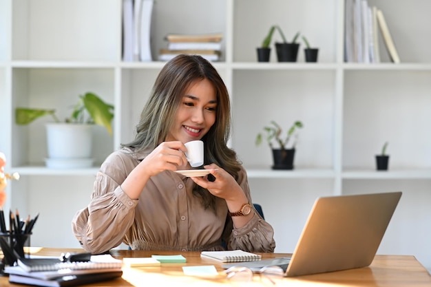 Thoughtful asian business woman drinking hot coffee and reading email on laptop computer