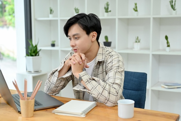 Thoughtful Asian man office worker working on his project on notebook laptop