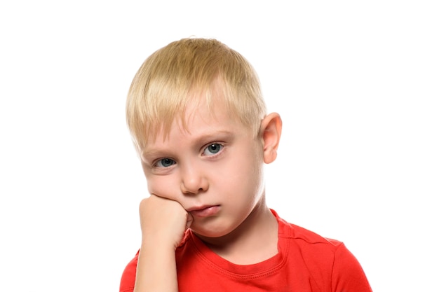 Thoughtful blond boy in a red T-shirt worth placing fist under his cheek