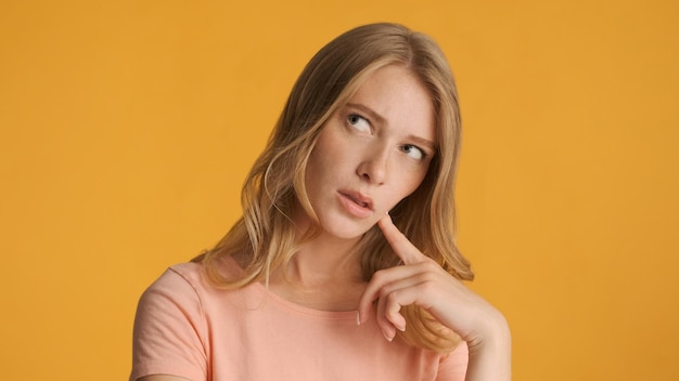 Thoughtful blond girl pondering on camera over colorful background Deep in thoughts expression