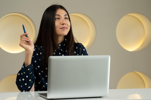 Thoughtful business asian woman working at a computer smiling and looking into the distance thinking