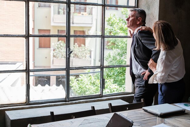 Thoughtful businessman looking out the window and his business partner giving her support Concept investment business failure