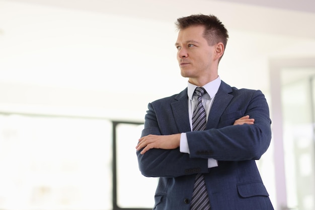 Thoughtful businessman with crossed arms looks aside in company office entrepreneur plans firm