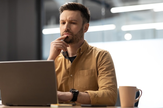 Thoughtful Businessman Working Online On Laptop In Modern Office