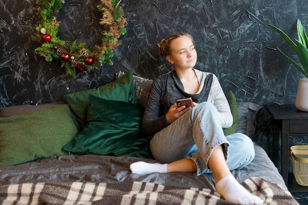 Thoughtful caucasian girl enjoying christmas eve at home using smart phone