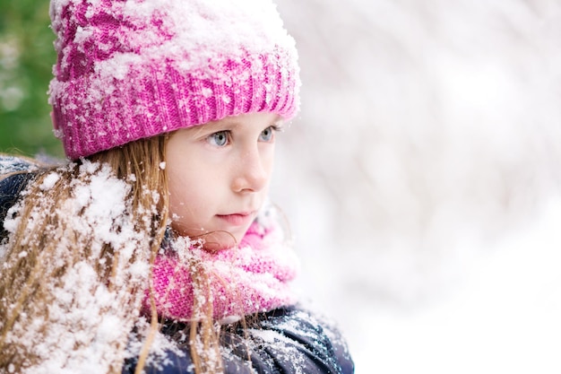 A thoughtful child in pink hat is gazing at something in winter