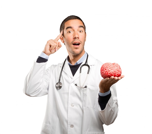 Thoughtful doctor holding a toy brain against white background