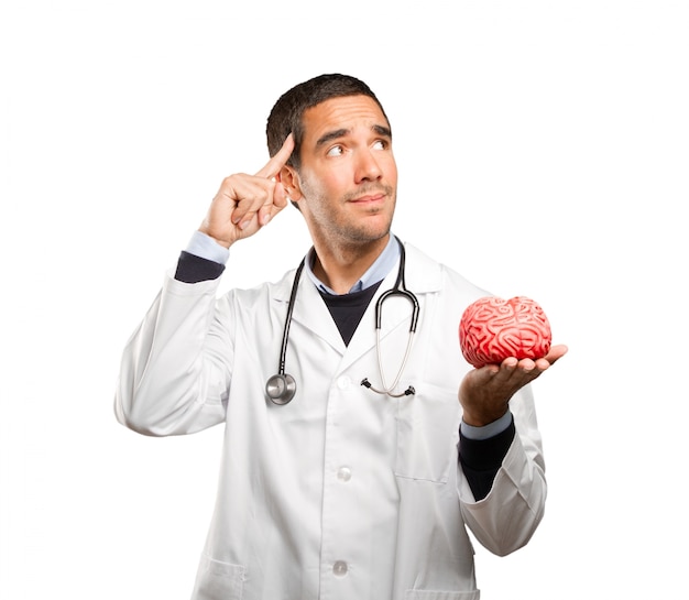 Thoughtful doctor holding a toy brain against white background