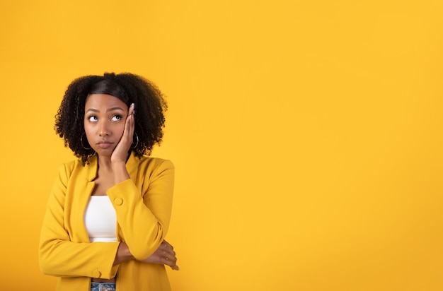 Thoughtful doubtful african american lady looking aside at copy space holding hand on cheek posing