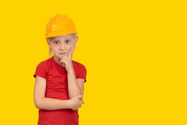 Thoughtful fairhaired boy in hard hat on yellow background Future career in construction