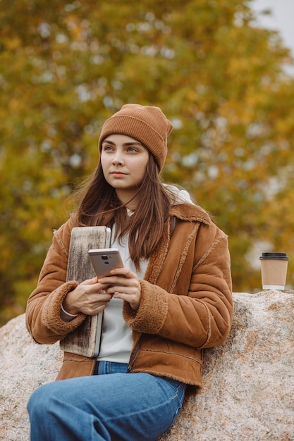 Thoughtful female freelancer with laptop using smartphone and thinking about project