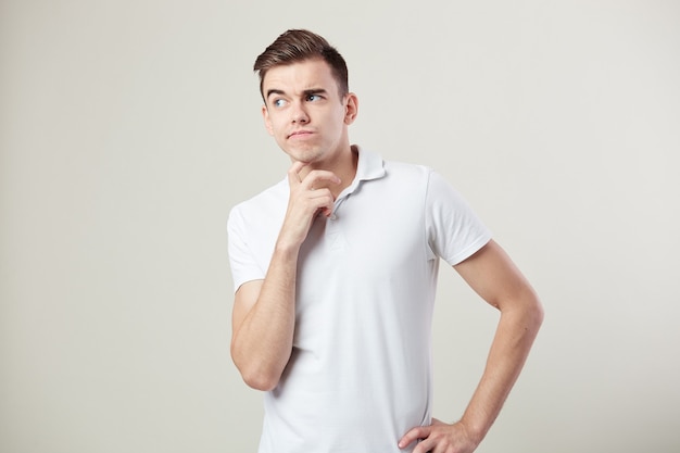 Thoughtful guy dressed in a white t-shirt and jeans is on a white background in the studio .