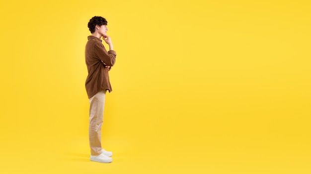 Thoughtful guy thinking looking aside at empty space yellow background