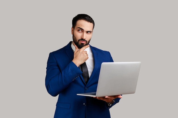 Thoughtful man holding laptop and thinking over startup strategy with serious doubtful expression