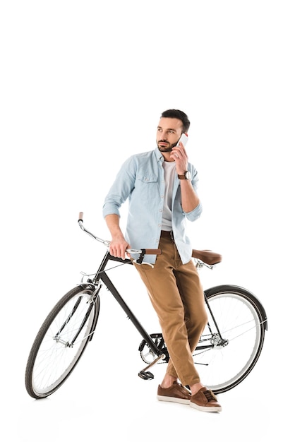 Thoughtful man with bicycle talking on smartphone and looking away isolated on white