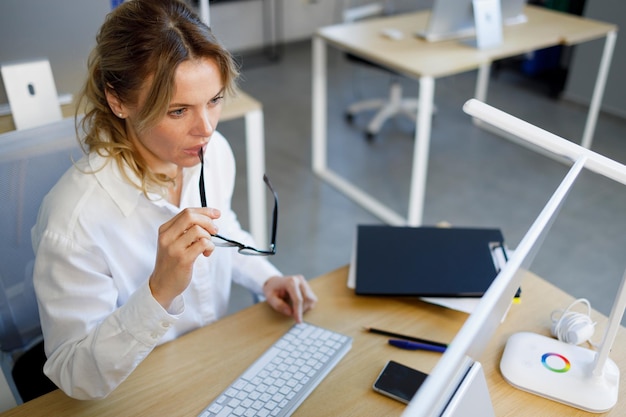 Thoughtful mature business woman is working on a computer at the workplace in office