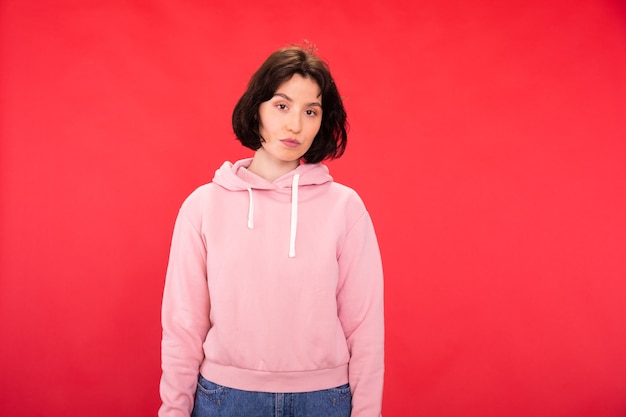 Thoughtful model in pink hoodie looking at front on red studio