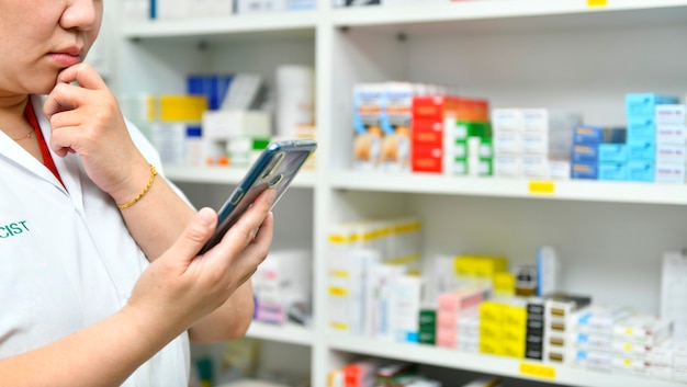 Thoughtful pharmacist holding mobile smart phone using for filling a prescription in pharmacy