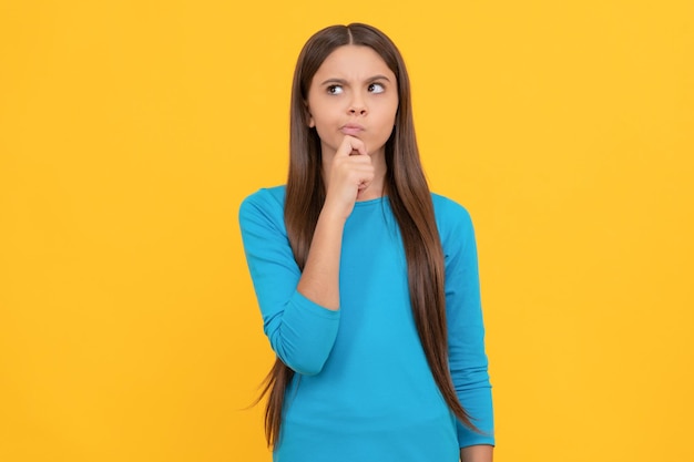 Thoughtful pretty look of young girl face portrait of child on yellow background