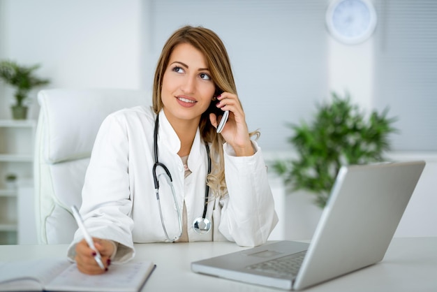 Thoughtful serious young female doctor lost in thoughts using smartphone, pondering question of diagnose.