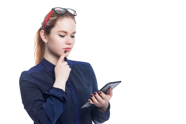 Thoughtful serious young redhaired woman in a blue blouse and glasses with a tablet Isolated on white background Space for text