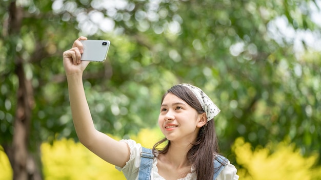 Thoughtful smile woman in park using smart phone for selfie photo Portrait of a young charming