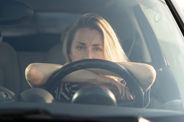 Photo thoughtful tired woman driving car looking through windshield at camera thinking about something