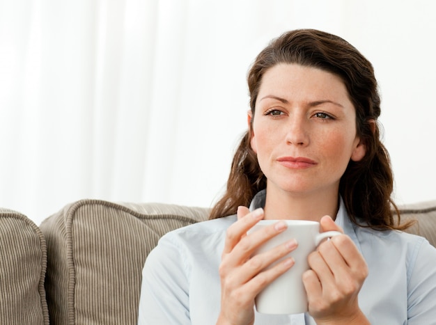 Thoughtful woman drinking coffee on the sofa